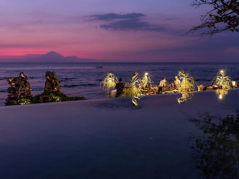 Wieczorny widok na oświetlony basen z morzem i górami w tle.