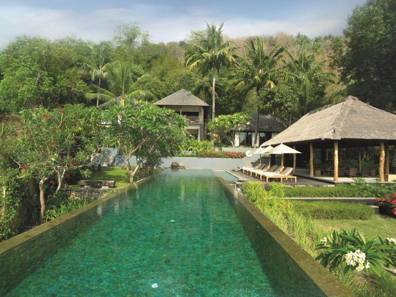 Widok na długi basen z zieloną wodą otoczony tropikalną roślinnością w ośrodku.