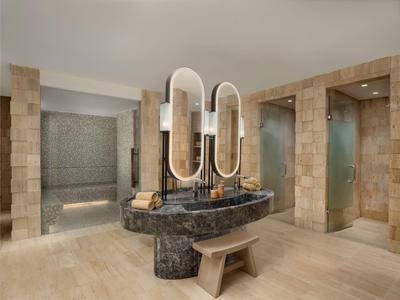Elegant bathroom with light wood floor, dark marble vanity, and two oval mirrors.