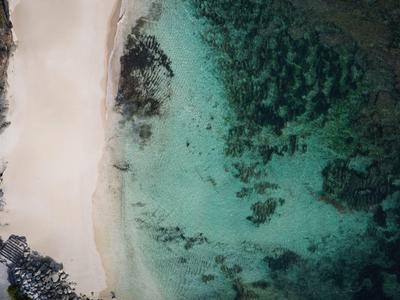 Aerial view of a white sandy beach with clear turquoise water and dark rocks.