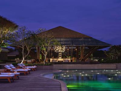 Evening view of a pool with lounge chairs and illuminated restaurant in the background