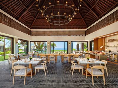 Elegant restaurant with wooden furniture, large windows, and views of the garden and sea.