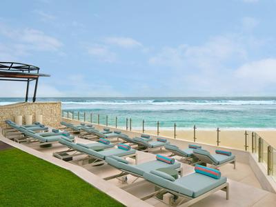 Rzędy leżaków z niebieskimi poduszkami na tarasie z widokiem na morze i plażę.