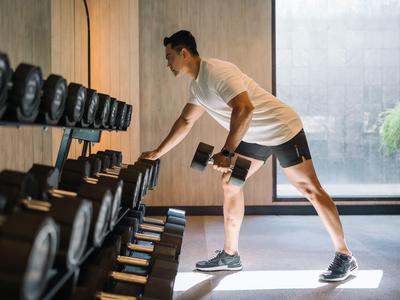 Mężczyzna ćwiczący z hantlem przed oknem w nowoczesnej siłowni.