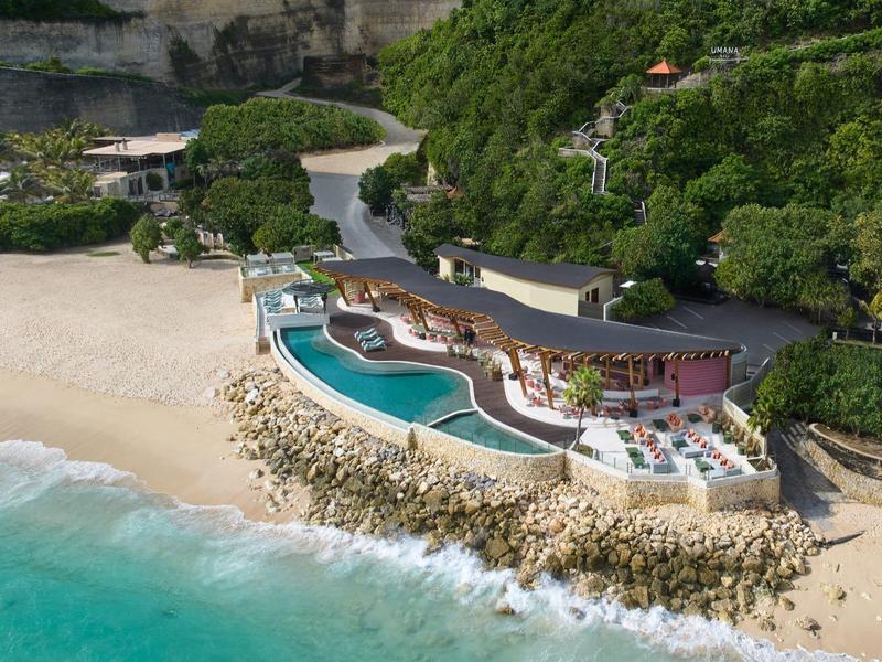 Luxury resort with pools on the beach, surrounded by green forest and cliffs.