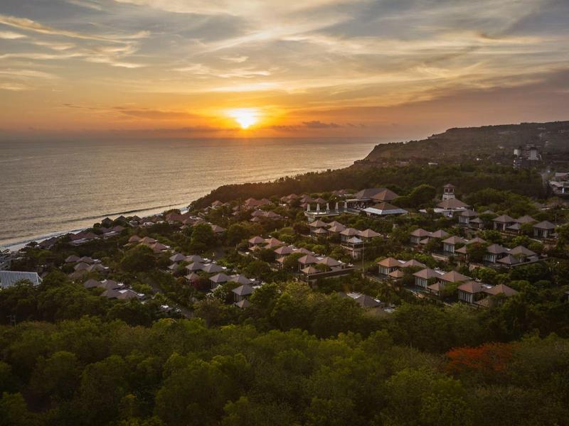 Sunset over a coastal town with lush greenery and calm sea.