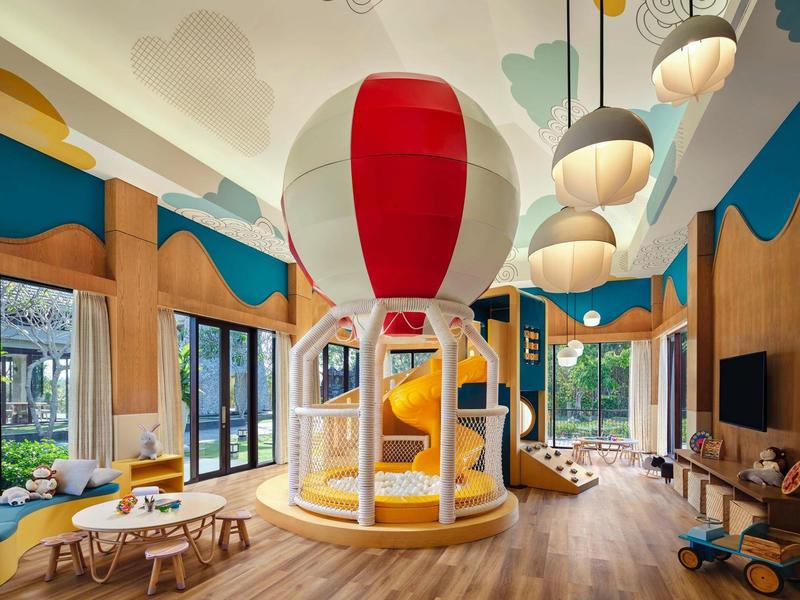 Indoor bright colorful children's play area with hot air balloon structure and wooden furniture.