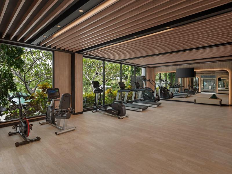Modern gym with equipment and large windows overlooking greenery.