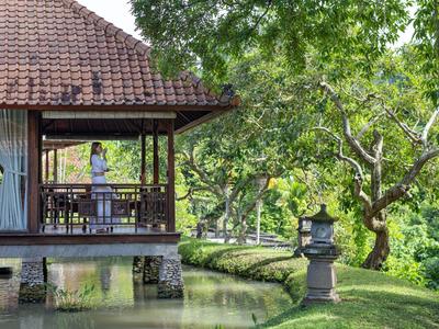 Zadaszony taras domu przy wodzie z drzewami i zielonym trawnikiem w tle