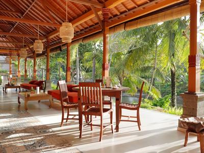 Véranda ouverte avec mobilier en bois et vue sur des plantes tropicales.