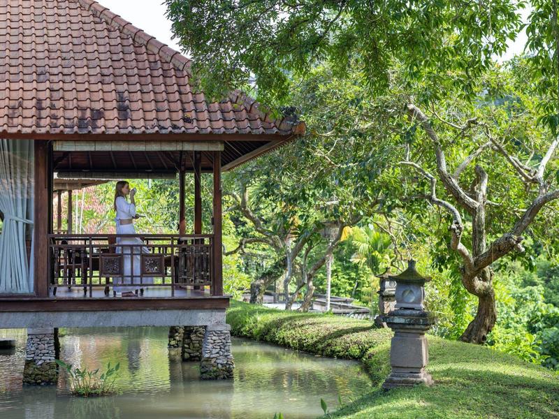 Restaurant en plein air sur pilotis au-dessus de l'eau avec un environnement vert luxuriant et des arbres.