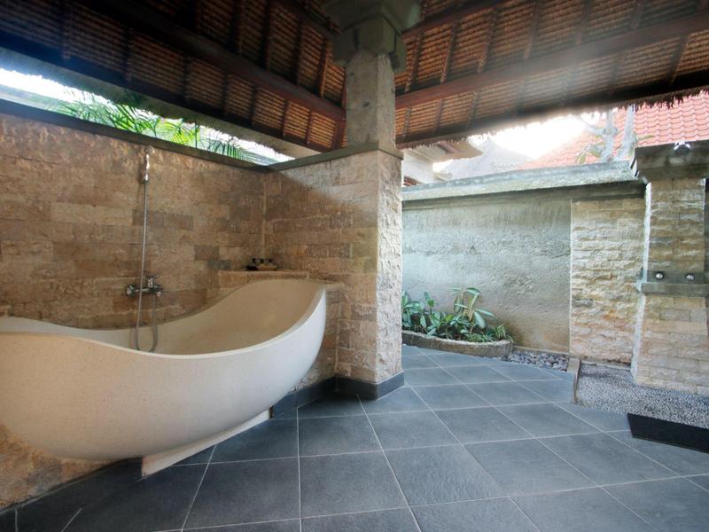 Salle de bain extérieure moderne avec baignoire indépendante et murs en pierre sous toit en bois.