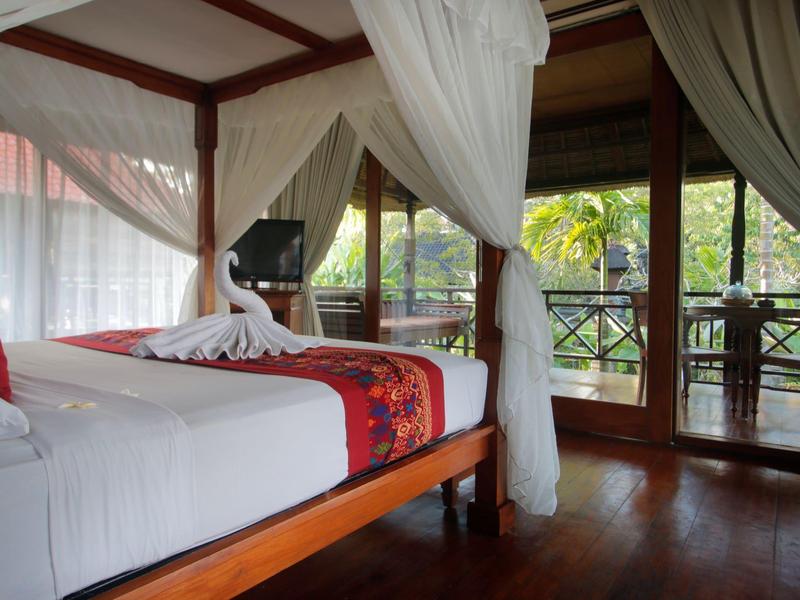 Chambre d'hôtel élégante avec lit à baldaquin, moustiquaires blanches et balcon avec vue sur le jardin.