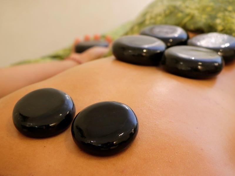 Cinq pierres noires lisses sont posées sur le dos d'une personne pour un massage aux pierres chaudes.