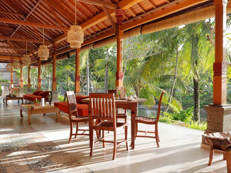 Véranda ouverte avec mobilier en bois et vue sur des plantes tropicales.