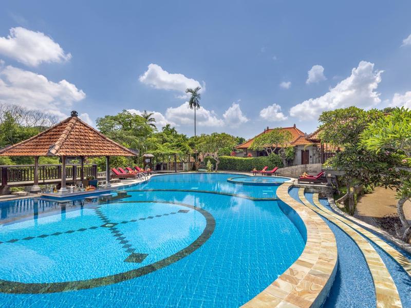 Grande piscine extérieure avec espaces de détente et végétation tropicale sous un ciel bleu