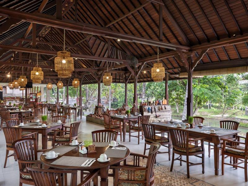 Salle à manger ouverte avec meubles en bois et luminaires suspendus en milieu tropical.