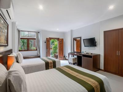 Jasny pokój hotelowy z dwoma łóżkami, drewnianymi szafami, telewizorem i balkonem z widokiem na zieleń.