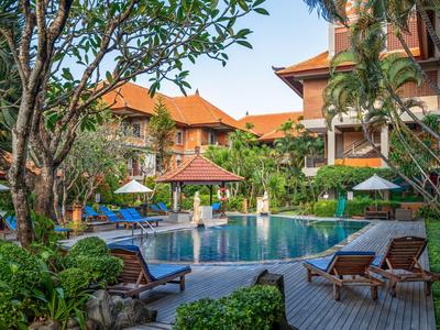 Poolbereich eines Hotels mit Liegestühlen, Sonnenschirmen und tropischer Vegetation.