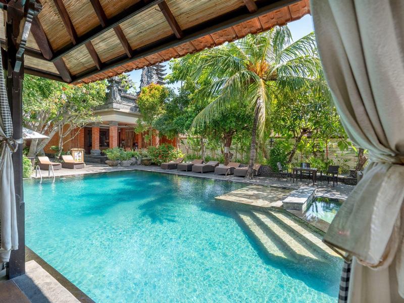 Widok na basen i tropikalne rośliny z zadaszonego tarasu hotelowego.