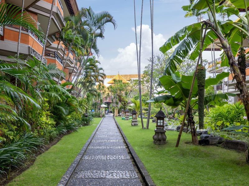 Wybrukowana ścieżka między tropikalnymi roślinami i palmami w kompleksie hotelowym.