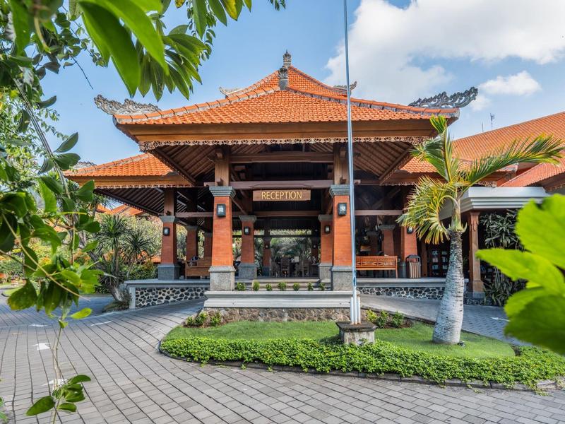 Tradycyjny balijski hotel z czerwonymi dachami i tropikalną roślinnością przy wejściu.
