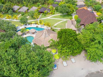 Luftaufnahme eines Resorts mit Pool, Bungalows und Liegestühlen am Strand.