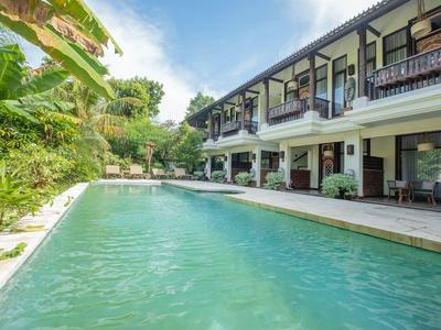 Nowoczesny basen hotelowy z otaczającymi roślinami i altankami pod błękitnym niebem.