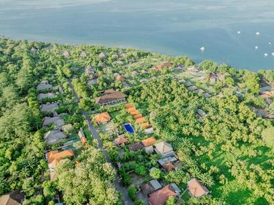 Luftaufnahme eines grünen Hotelresorts nahe am Wasser mit vielen Gebäuden und Booten im Hintergrund.