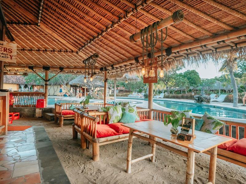 Offener Restaurantbereich mit rotem Polstersitz und Holztischen mit Blick auf einen Pool.