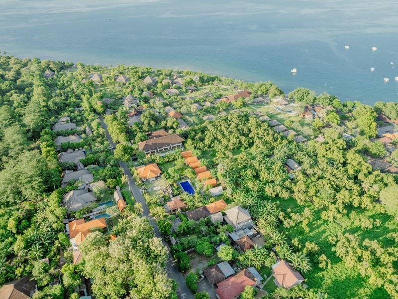 Luftaufnahme eines grünen Hotelresorts nahe am Wasser mit vielen Gebäuden und Booten im Hintergrund.