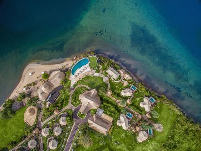 Veduta aerea di un resort sulla spiaggia con diverse capanne rotonde e piscine vicino al mare.
