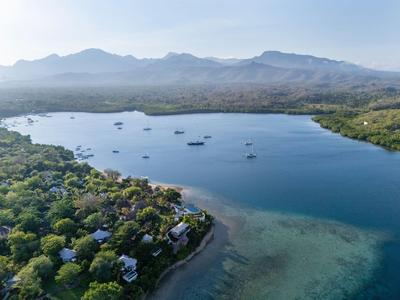 Baia con acqua limpida e blu circondata da colline verdi e montagne sullo sfondo.