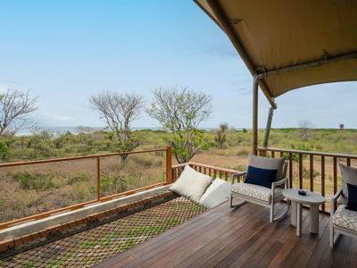 Balcone con sedie, cuscini e tavolo con vista sulla boscaglia sotto un cielo azzurro.