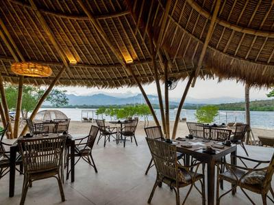 Otwarta jadalnia pod strzechą z widokiem na basen i krajobraz.