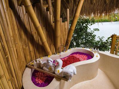 Vasca da bagno con petali di fiori davanti a parete di bambù con vista sul verde