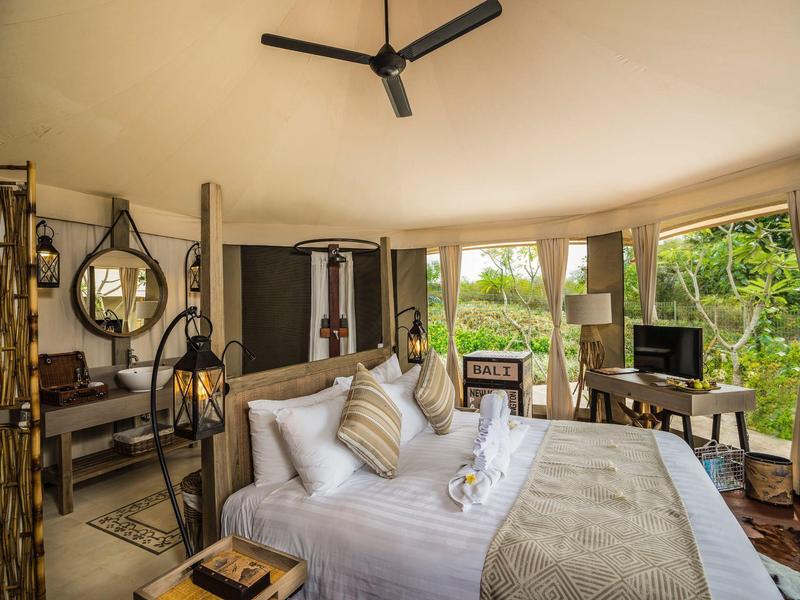 Camera d'hotel accogliente con letto grande, ventilatore a soffitto e vista sulla natura.