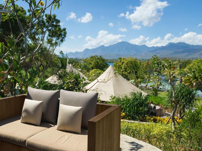 Panchina comoda con cuscini su una terrazza, circondata dal verde con montagne e cielo sullo sfondo.