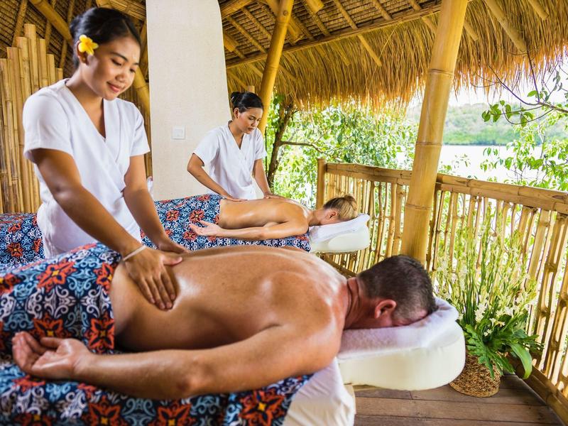 Due persone ricevono un massaggio alla schiena in una capanna per massaggi aperta con pareti di bambù.