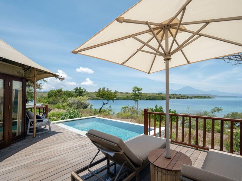 Terrazza con piscina, lettini e vista sul mare e le montagne sotto un cielo sereno.