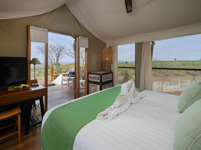 Camera luminosa con letto matrimoniale, copriletto verde e vista su terrazza e paesaggio.