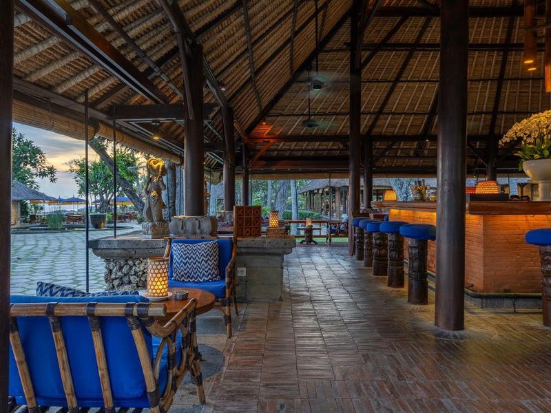 Open hotelbar met houten meubels en zeezicht bij zonsondergang.