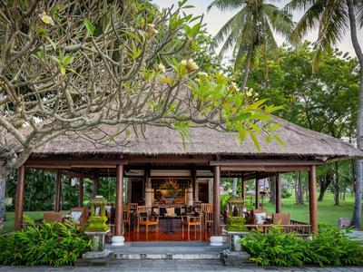 Open paviljoenrestaurant met houten meubels in tropische tuin met palmbomen.