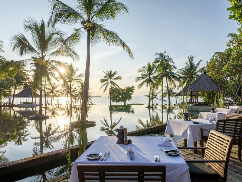 Essbereich im Freien mit Blick auf Palmen und Wasser bei Sonnenaufgang.