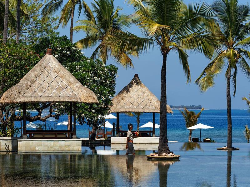 Pavillons und Palmen am Wasser mit Blick auf das Meer an einem sonnigen Tag