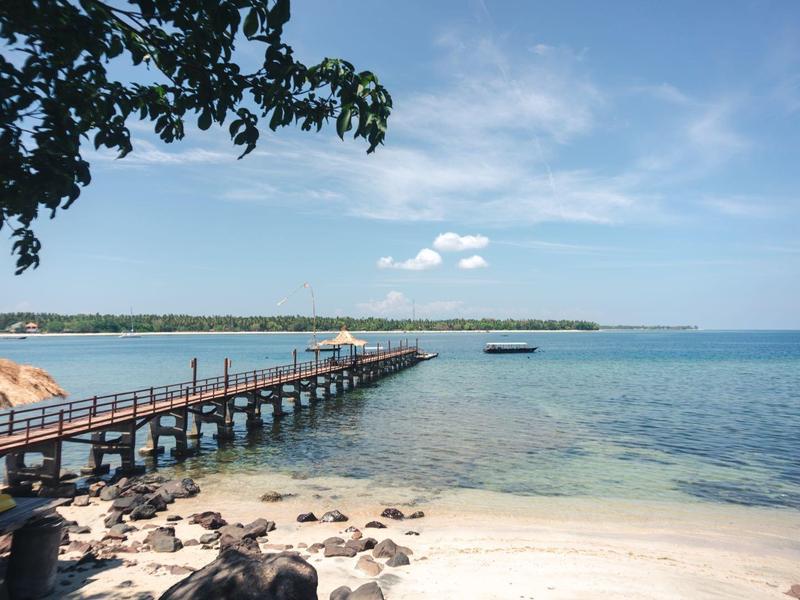 Ein Steg an einem tropischen Strand mit klarem Wasser und blauem Himmel.