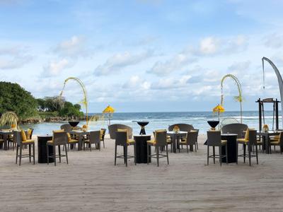 Ristorante all'aperto con tavoli e sedie su una terrazza in legno con vista sul mare e cielo blu.