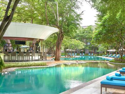 Piscina con acqua turchese, ombrelloni e posti a sedere in un giardino verde dell'hotel.