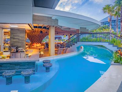 Piscina moderna in hotel con bar in acqua, circondata da palme e area lounge.