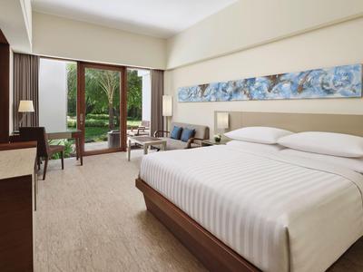Camera d'hotel con letto grande, due poltrone, scrivania e balcone con vista sul giardino.